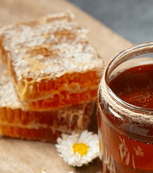 Slabs of capped raw honeycomb next to a jar of honey